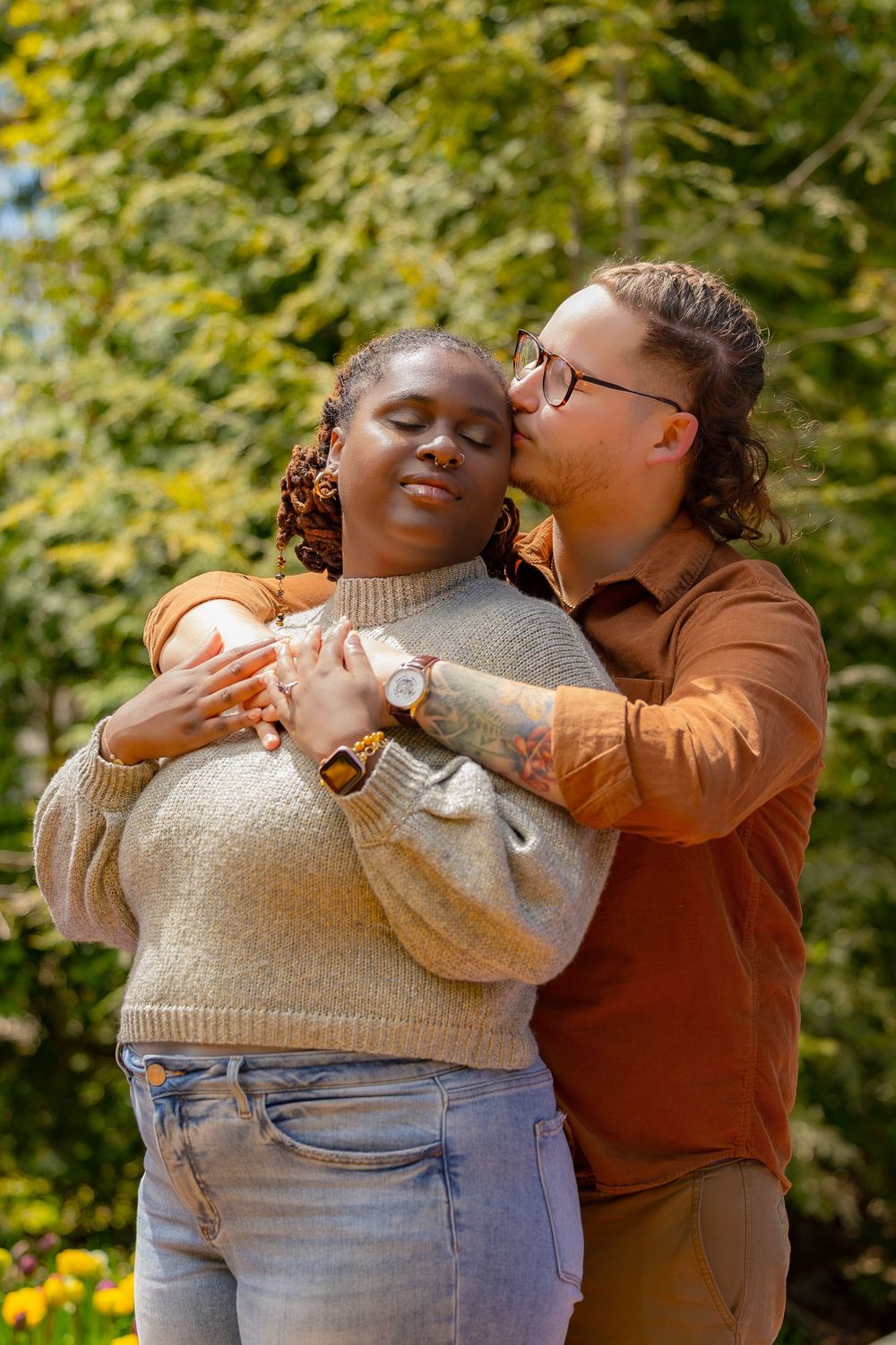 A loving couple embraces outdoors on a sunny autumn day wearing cozy sweaters against a backdrop of golden foliage.