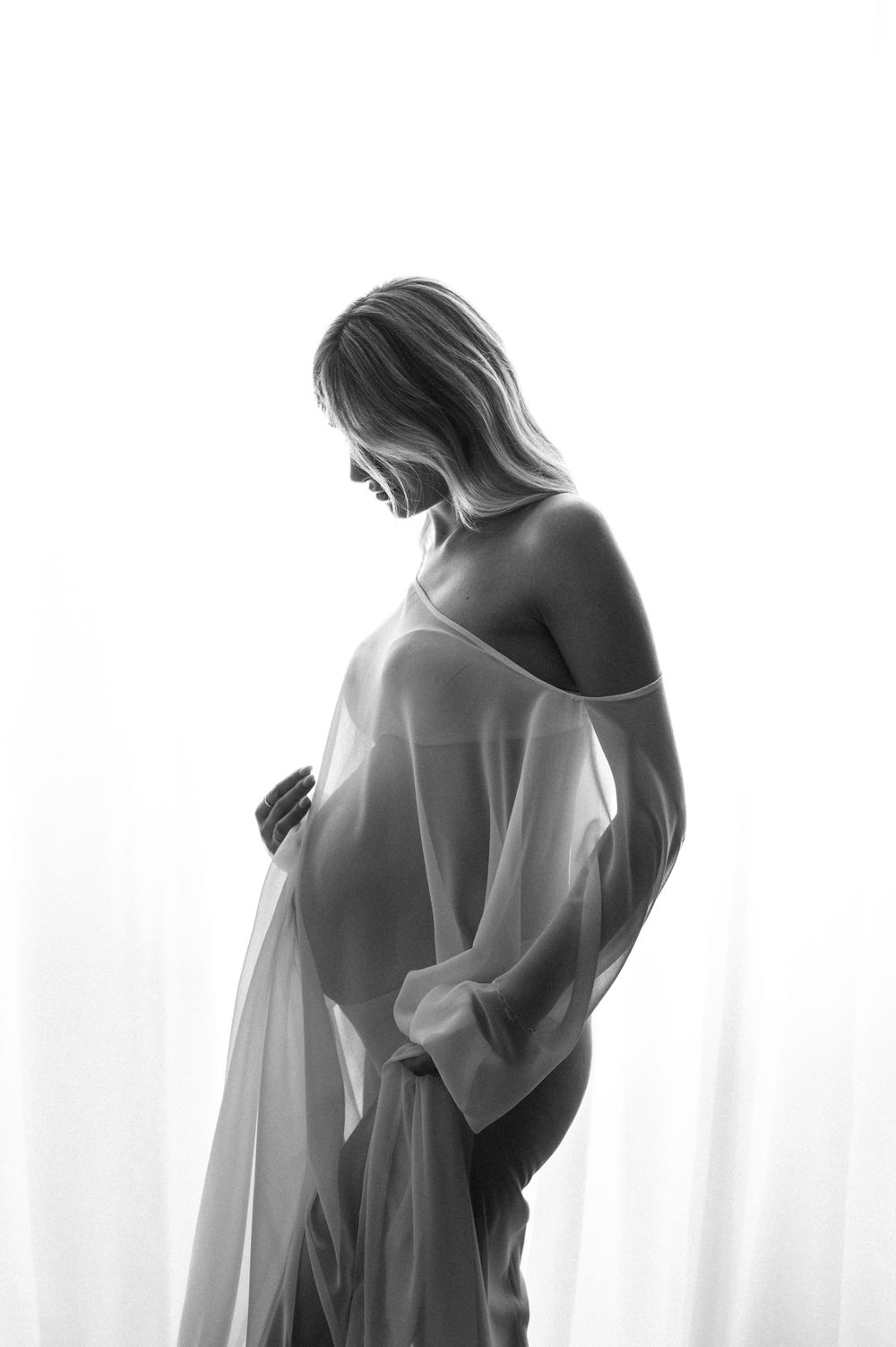 Artistic black and white silhouette of an expectant mother in flowing fabric.