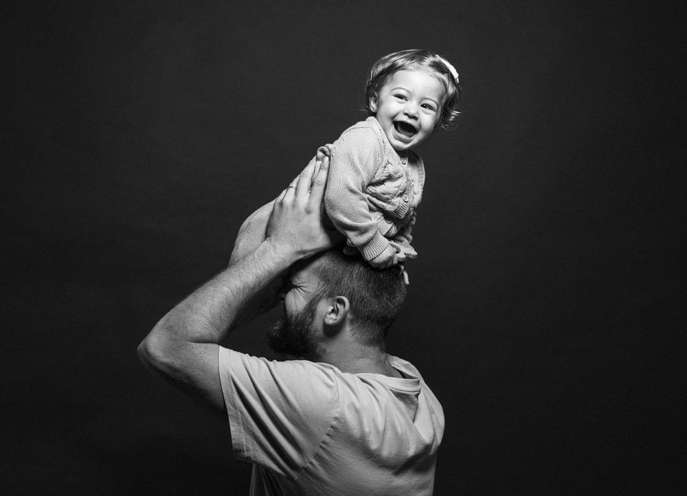 Ritratto in bianco e nero del padre che solleva il bambino gioioso sopra la sua testa su sfondo scuro.