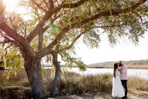 A couple stands under a large oak tree during a romantic sunset photo session in a coastal marsh setting. Summerville/Charleston, SC