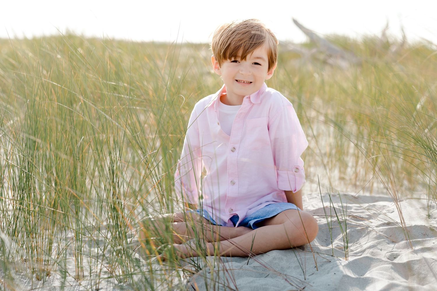 Child sits peacefully among tall beach grass on sandy dunes during golden hour.
