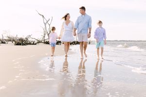 A family walks together along a white sandy beach with gentle waves rolling in at sunset.
