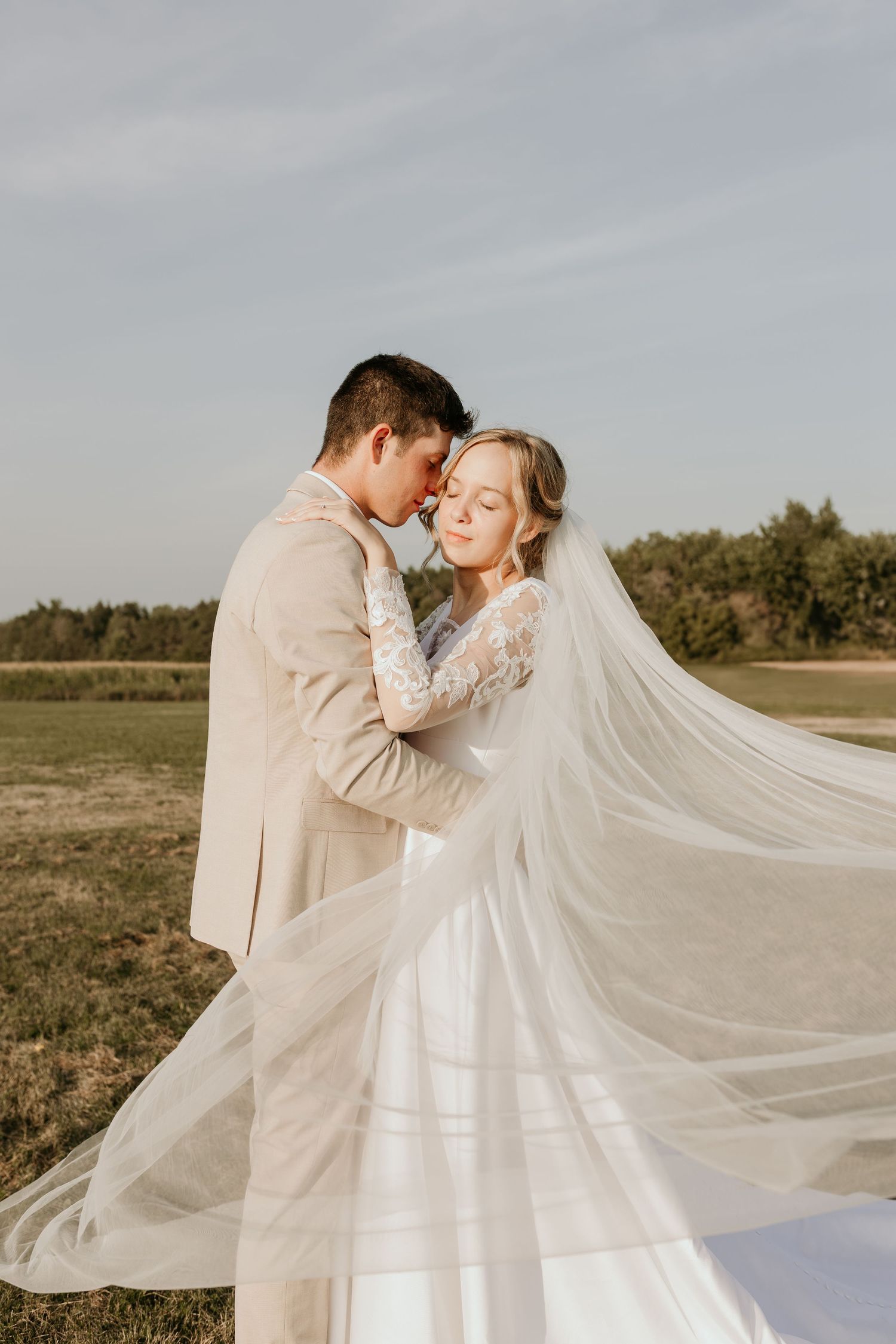 Romantic wedding portrait with elegant white dress and pastel floral bouquet in woodland setting.