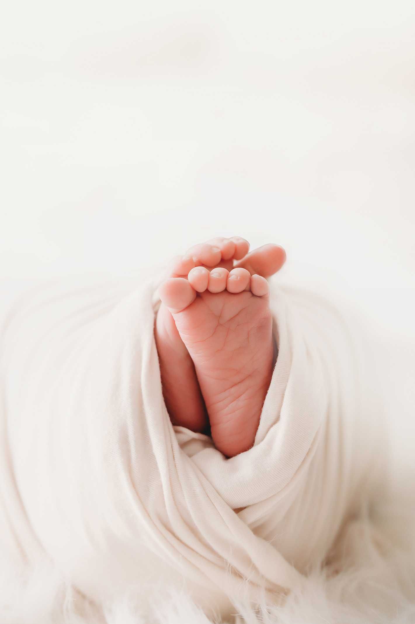 A tiny baby foot wrapped in soft white fabric, showing delicate toes against a light background.