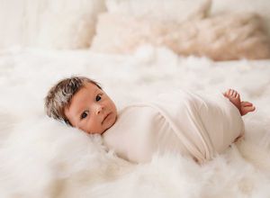 Baby wearing white onesie lying on soft white blanket during newborn photo session.