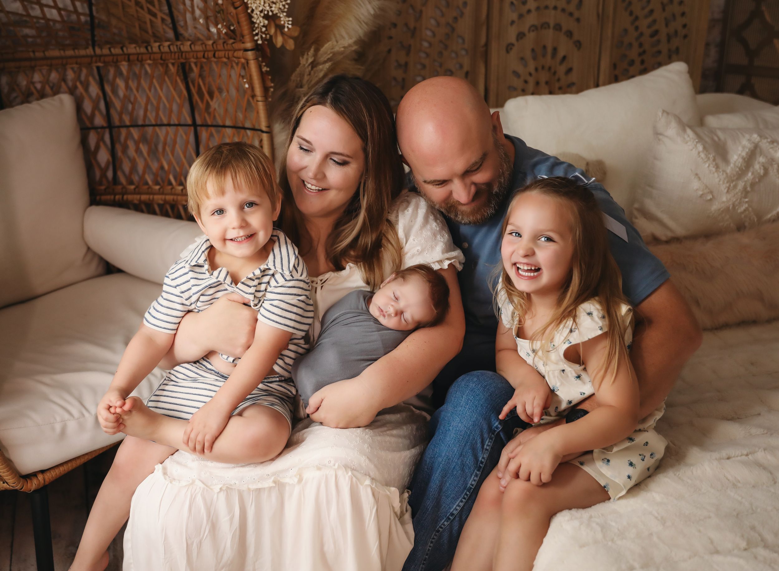 A happy family of five poses on a couch, including a newborn baby, two young children, and smiling parents.