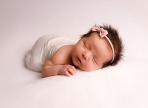 A peaceful sleeping newborn baby lies on soft white fabric in a minimalist studio setting.