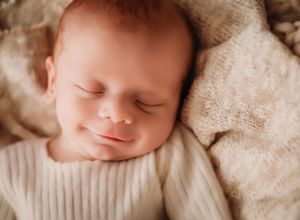 A sleeping baby in a cozy cream-colored knit sweater rests peacefully against a soft beige blanket.