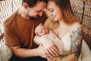 A tender family moment as parents cradle their newborn baby while sitting together in warm natural light.