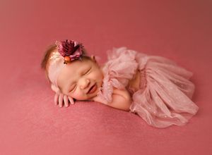 A baby in a pink tulle dress lies on a soft pink backdrop during a professional newborn photo session.