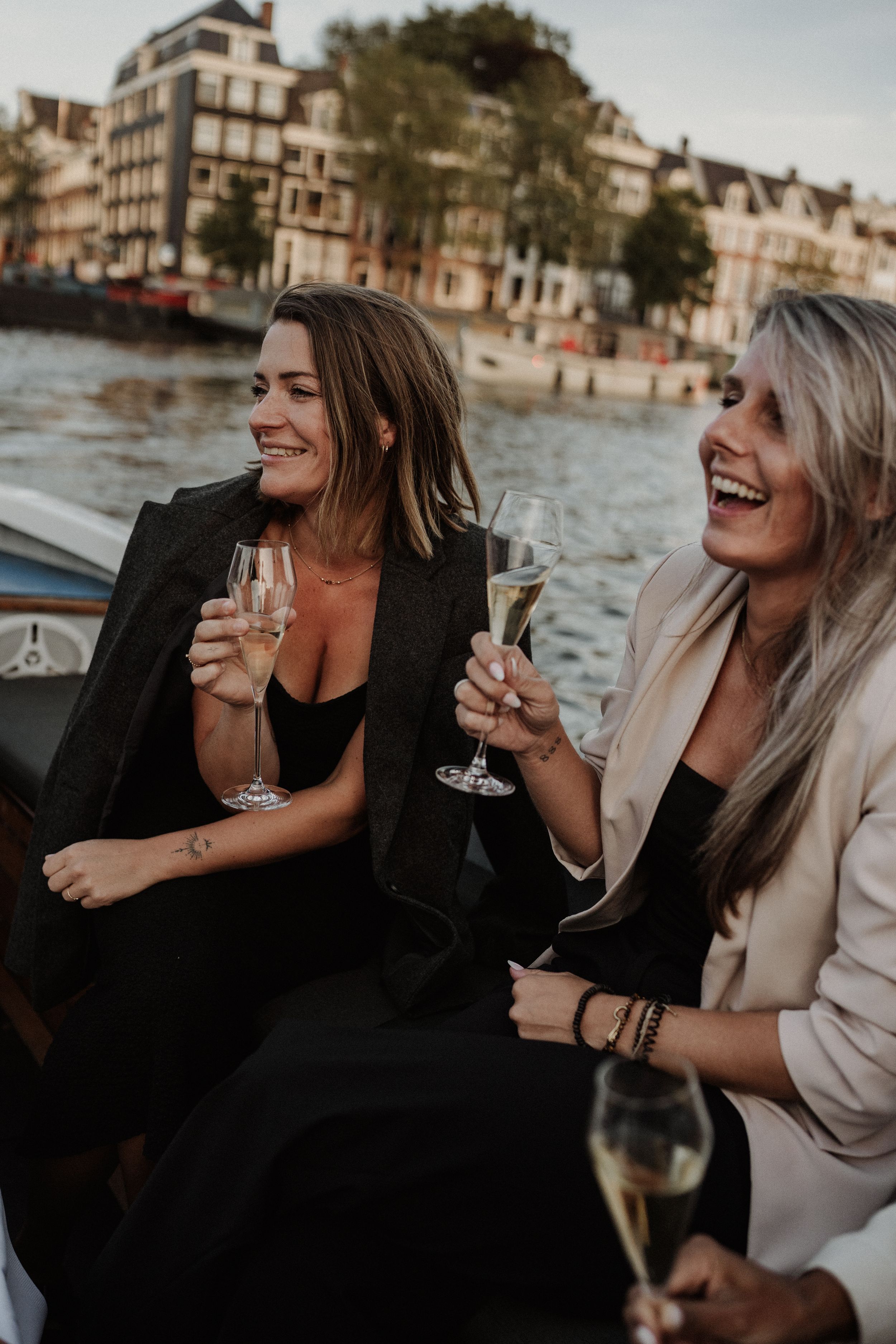 Two friends enjoying champagne and laughing together on a boat in Amsterdam's canals at sunset.