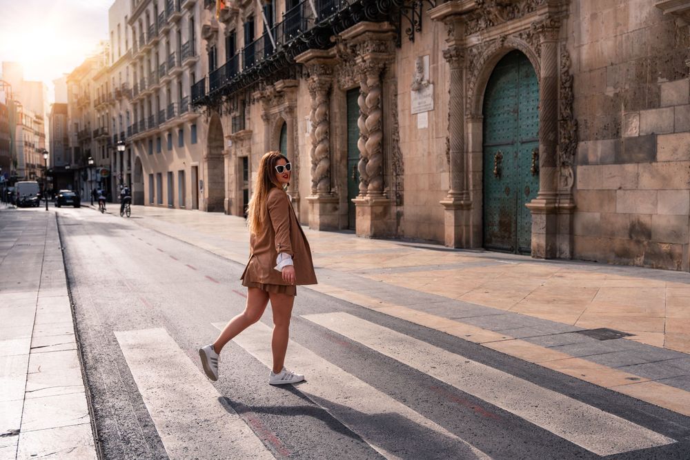 young woman crossing the street with sunsetting behind her and lifestyle casual photo in Alicante Spain