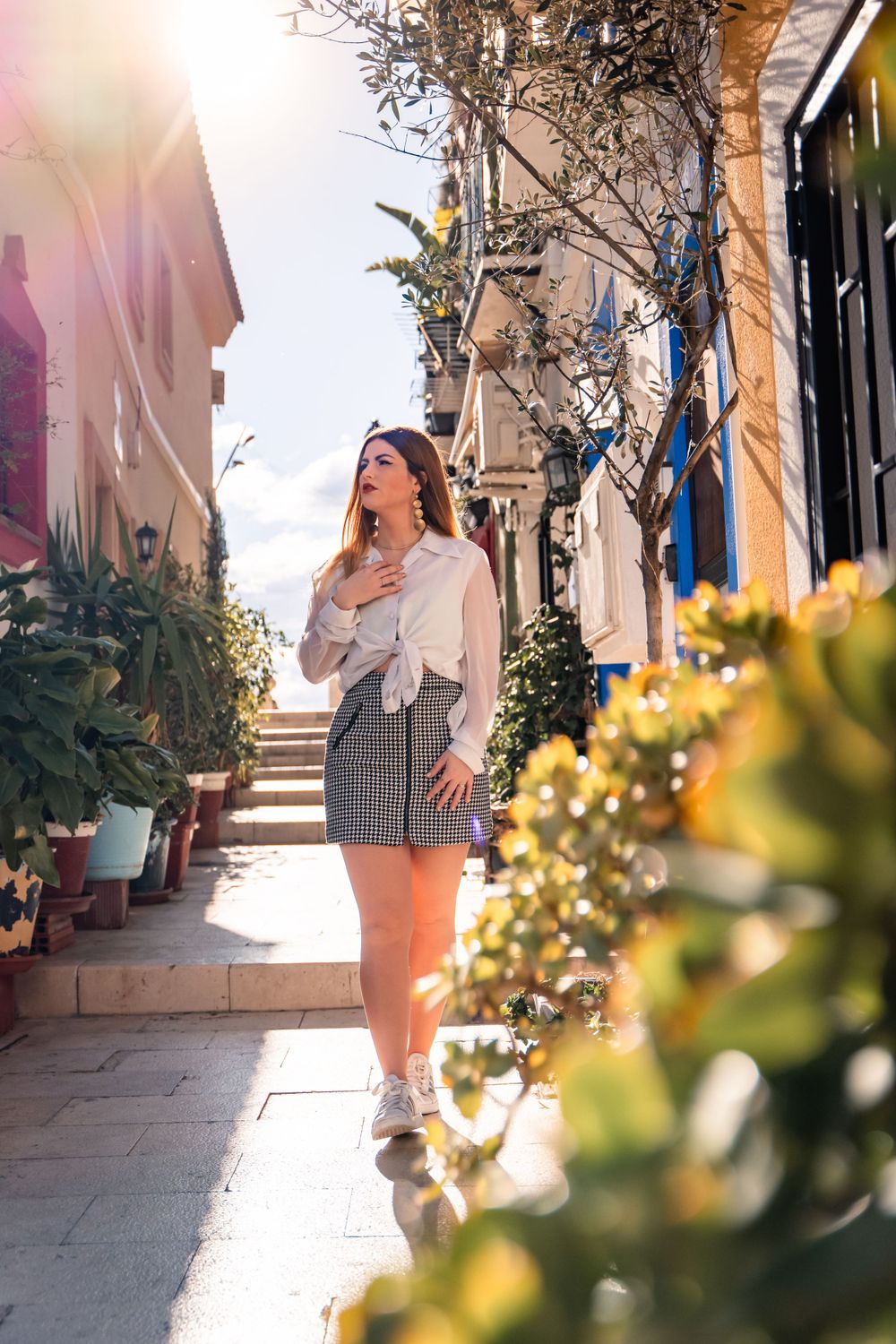 Woman walking through the narrow and colourful streets in Barrio De Santa Cruz Alicante with golden sun behind her