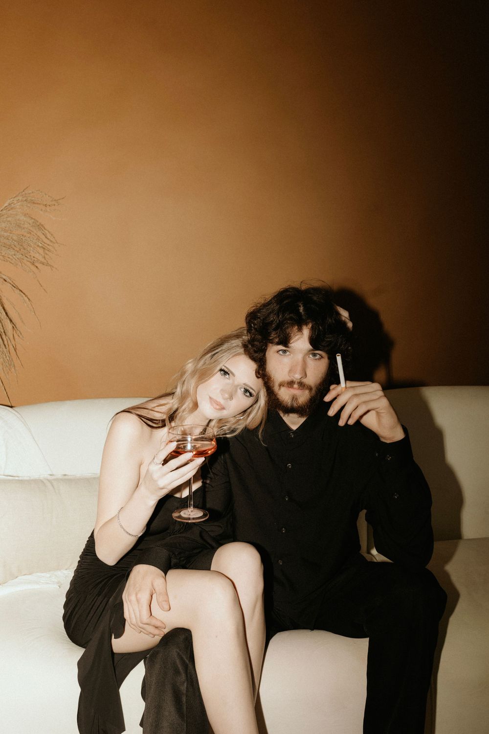 Intimate portrait of couple relaxing with drinks on white sofa.
