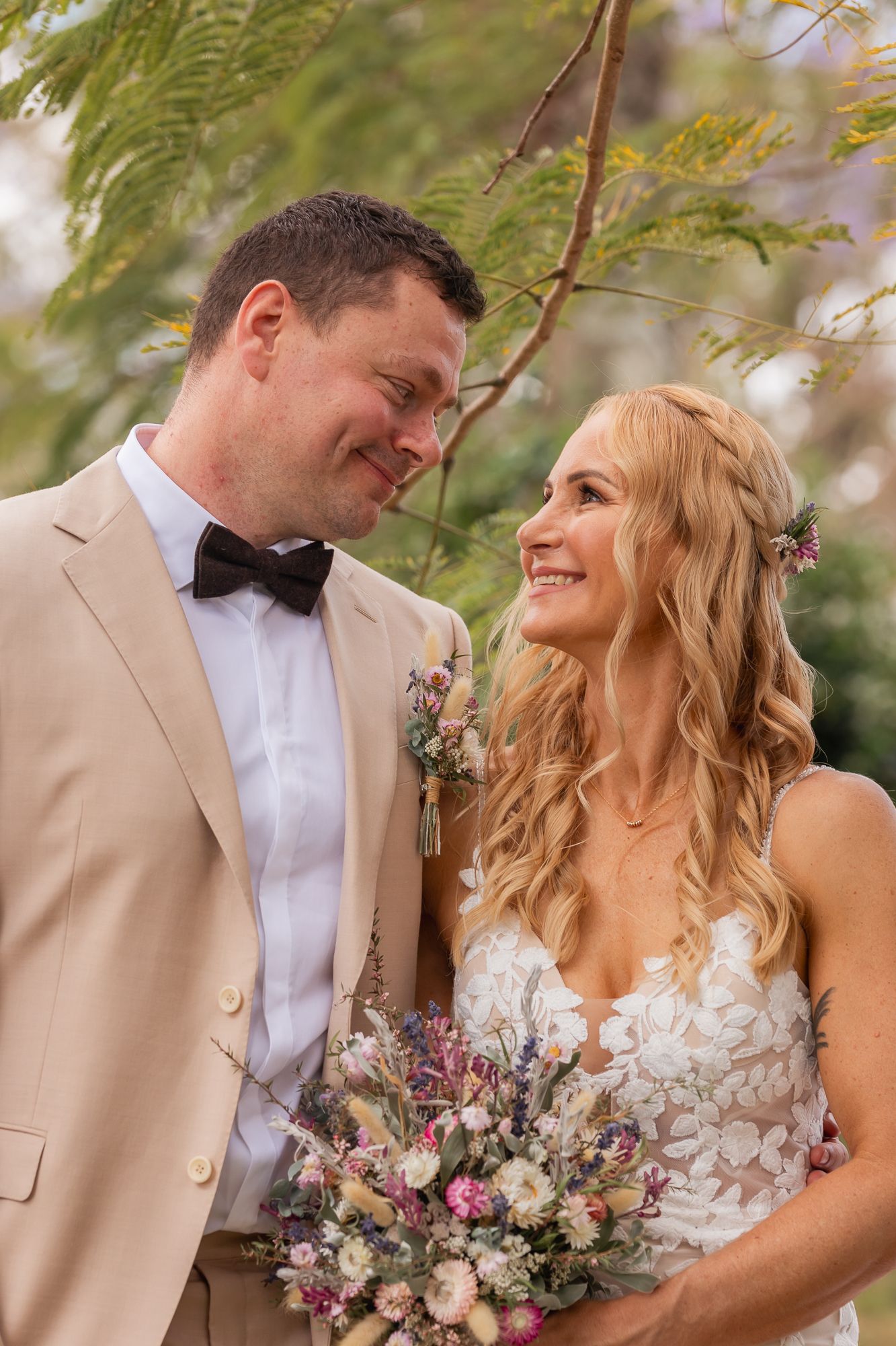 Elegant wedding couple posing outdoors with pink and purple floral bouquet.