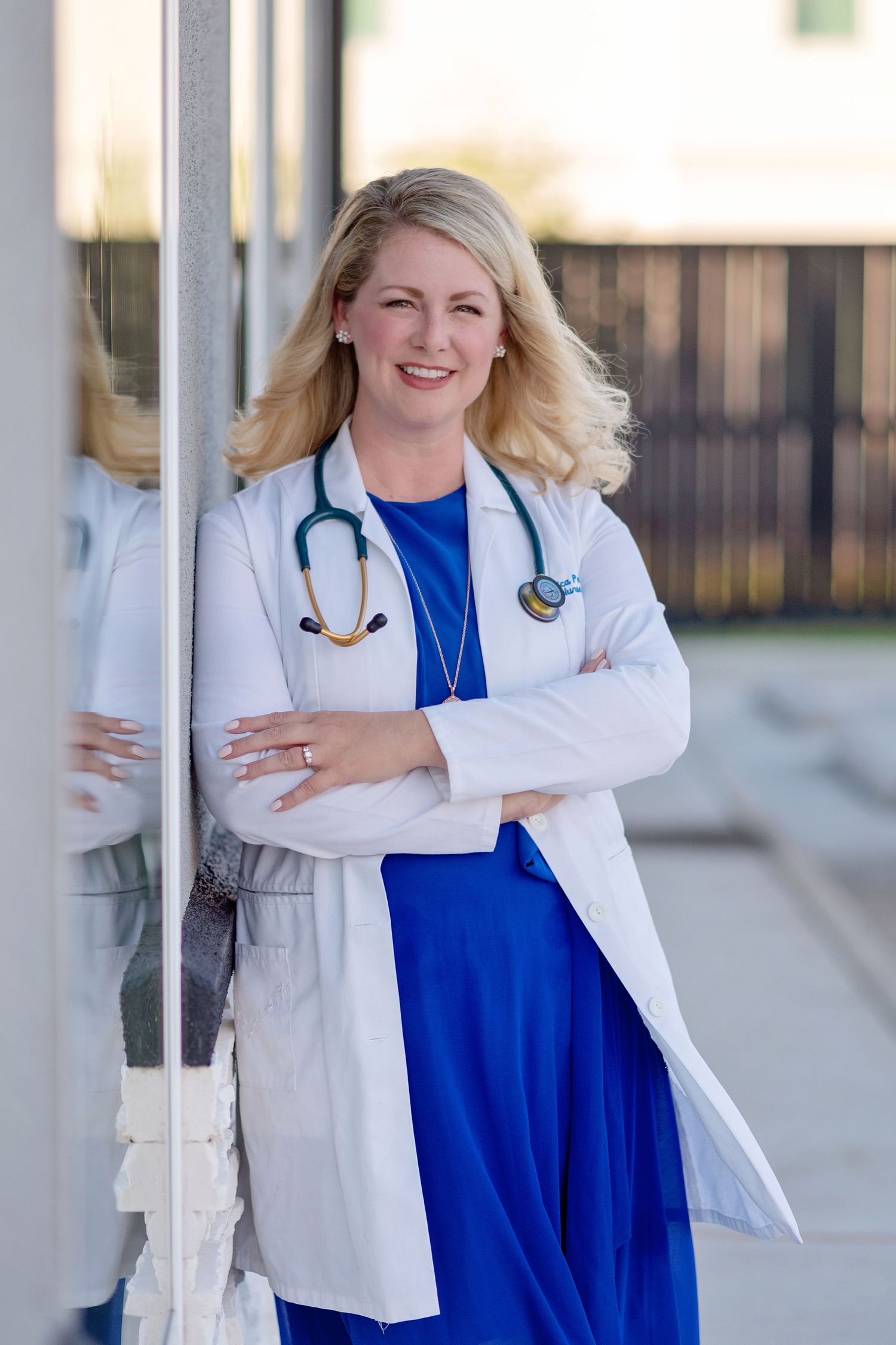 headshot of smiling nurse practitioner leaning against wall wearing white coat and stethoscope