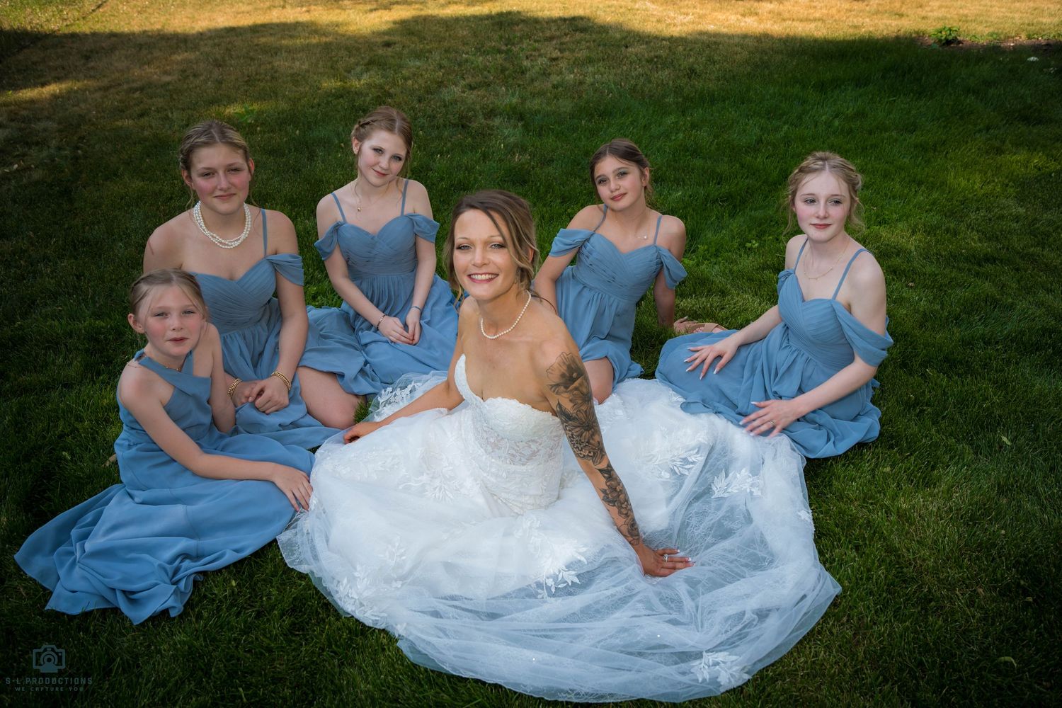 A bride stands with her bridesmaids, all dressed in matching attire, smiling and posing for a photo together