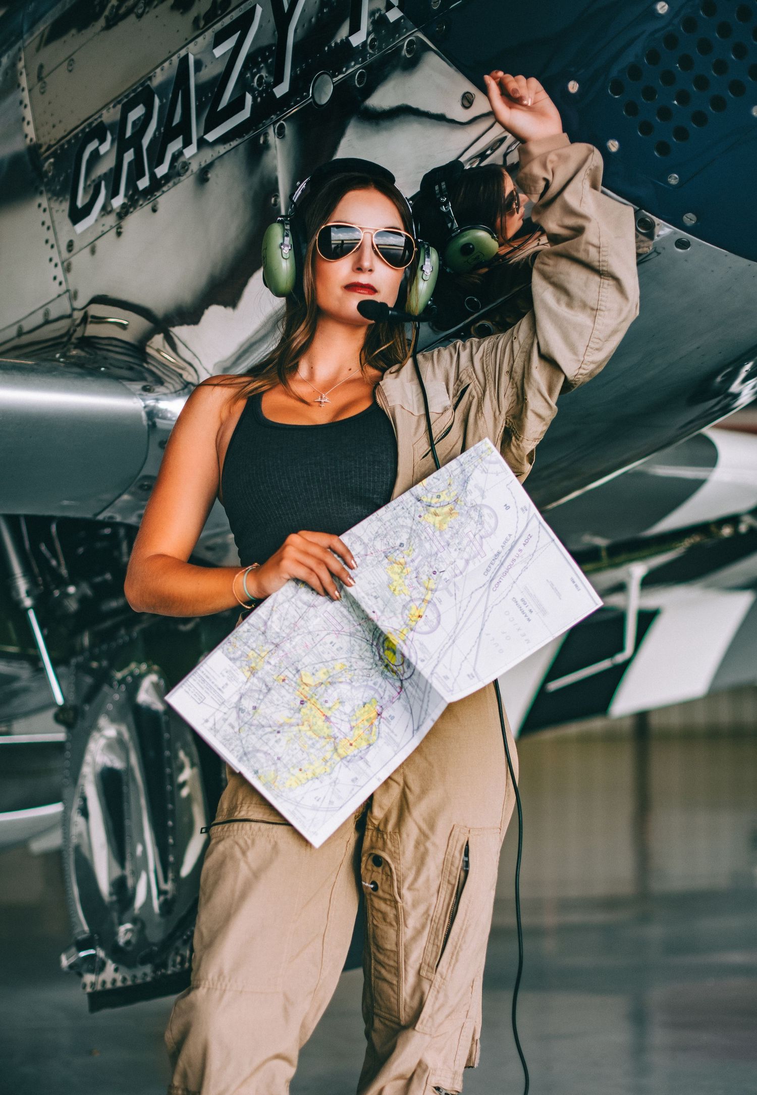 Pilot in sunglasses and aviator headset studies navigation map while standing next to aircraft.