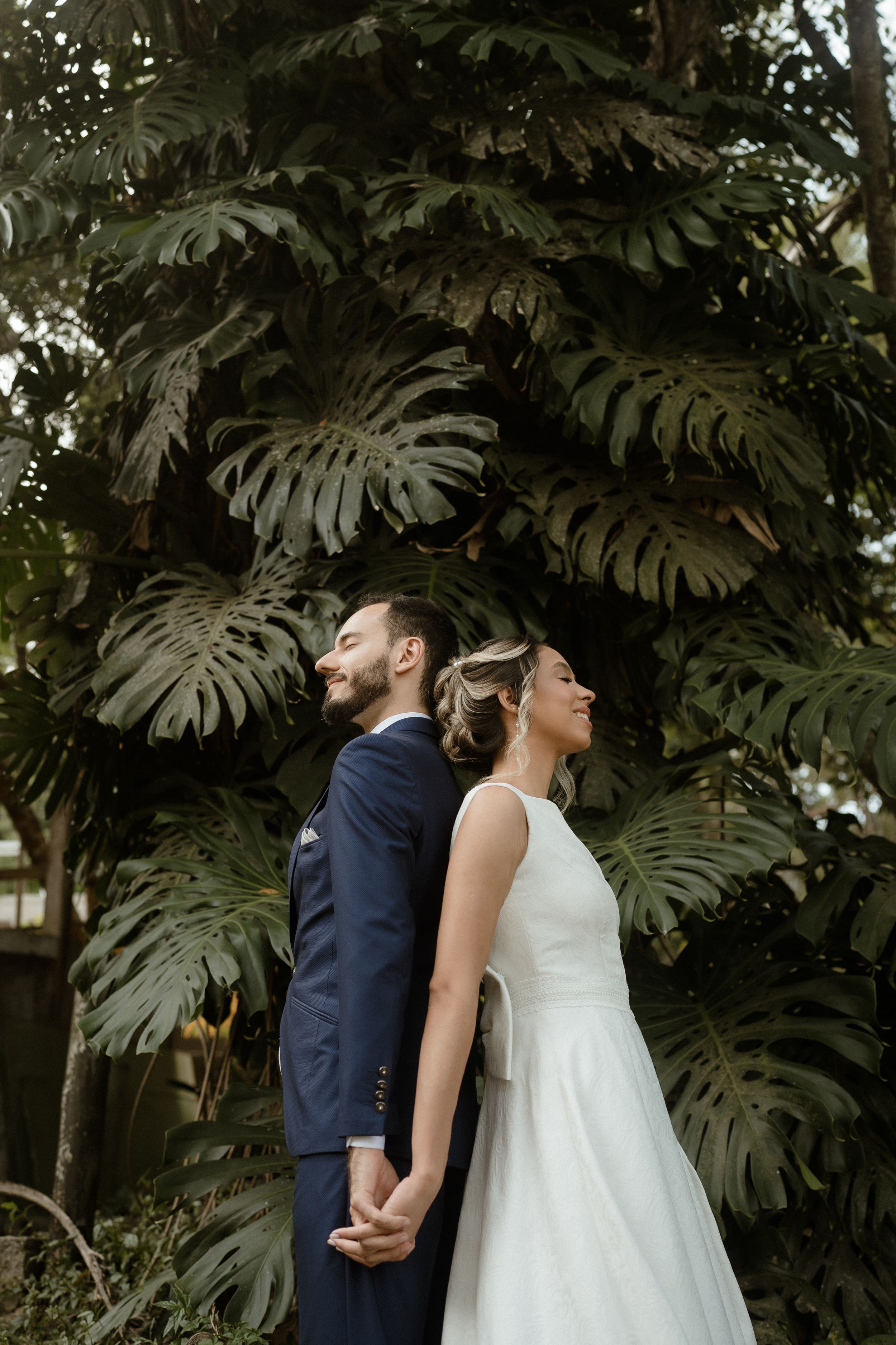 Wedding couple stands back-to-back against a backdrop of dramatic tropical foliage.
