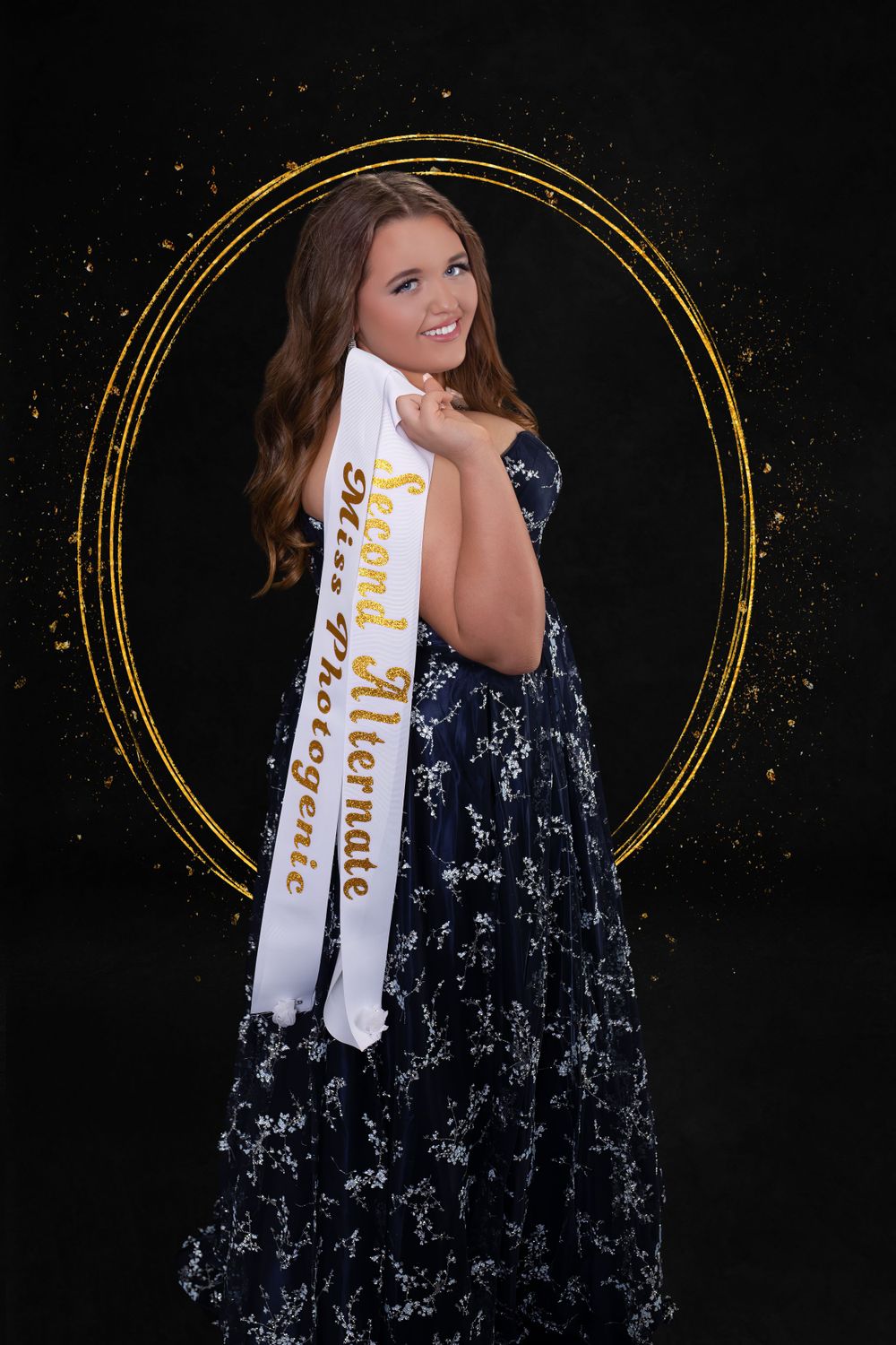 Pageant contestant poses with white sash against black background with decorative gold circular frame.