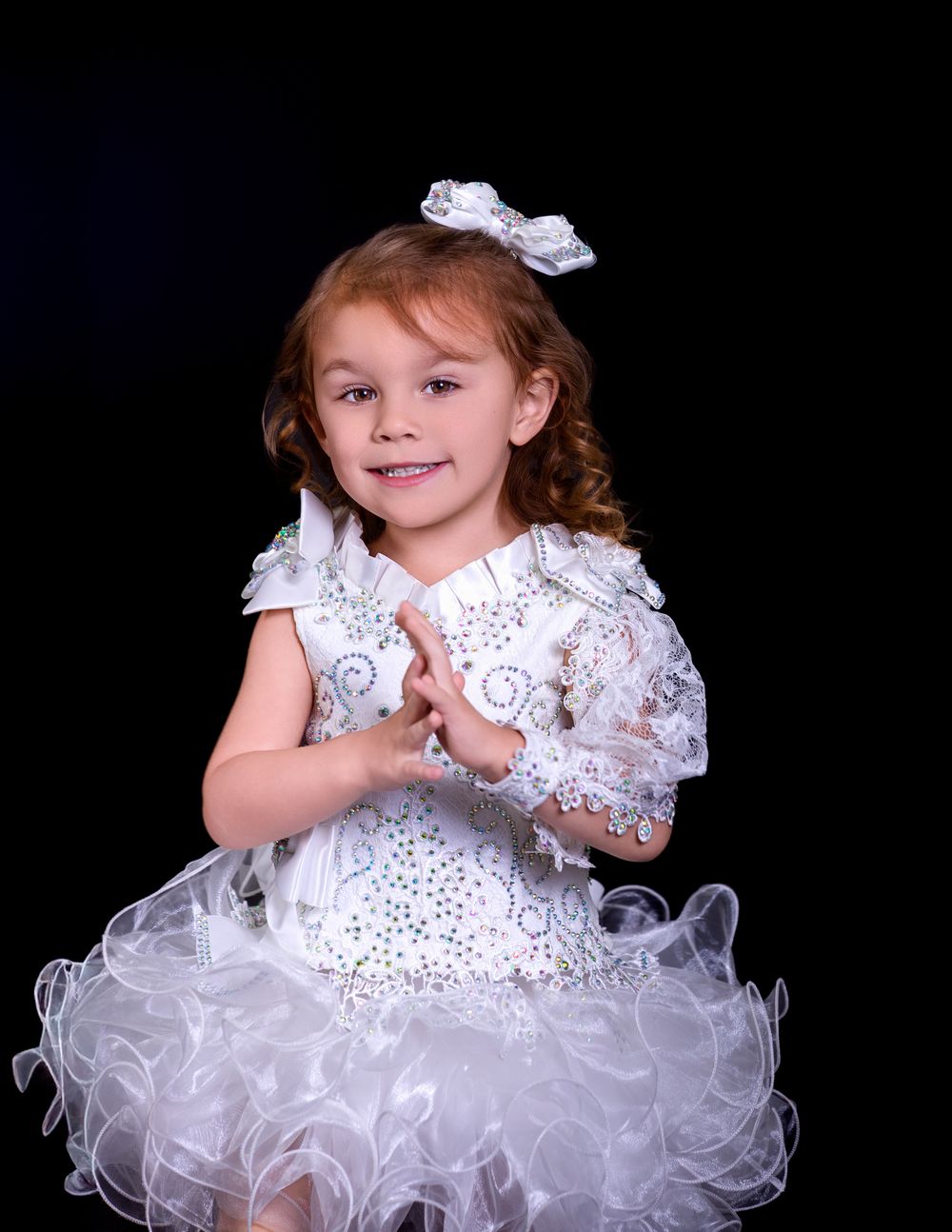 Studio portrait in white lace dress and hair bow against dark background.