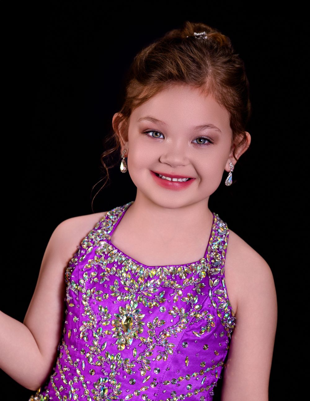 Portrait against black background showing a bright smile and sparkly purple dance costume with beaded details.