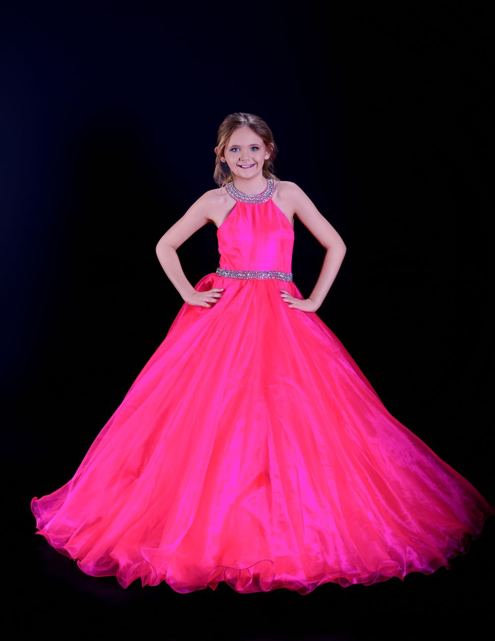 Child wearing a vibrant hot pink ball gown twirls on dark stage showing the flowing tulle layers of the dress.