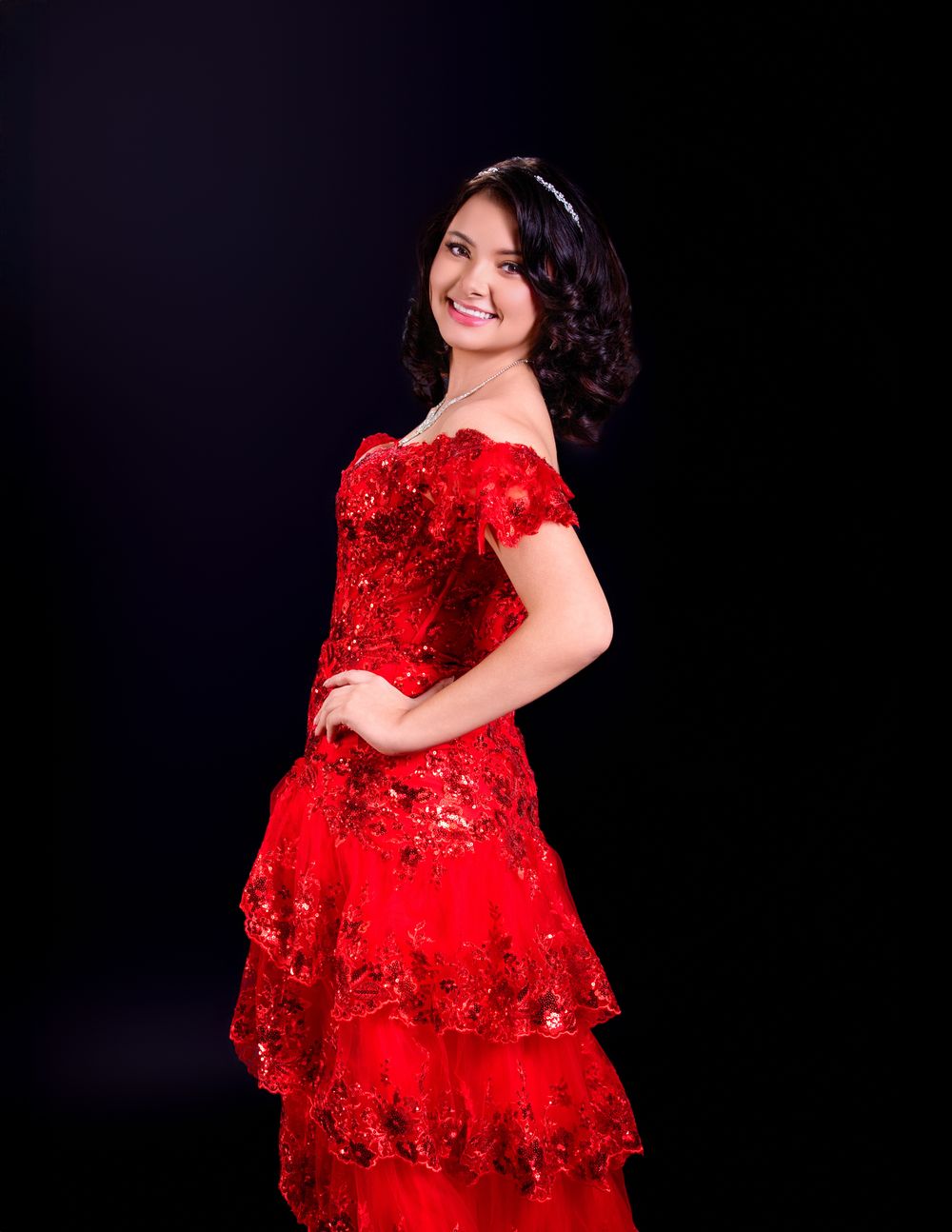 A woman posing in a stunning red sequined evening gown with tiered layers against a black background.