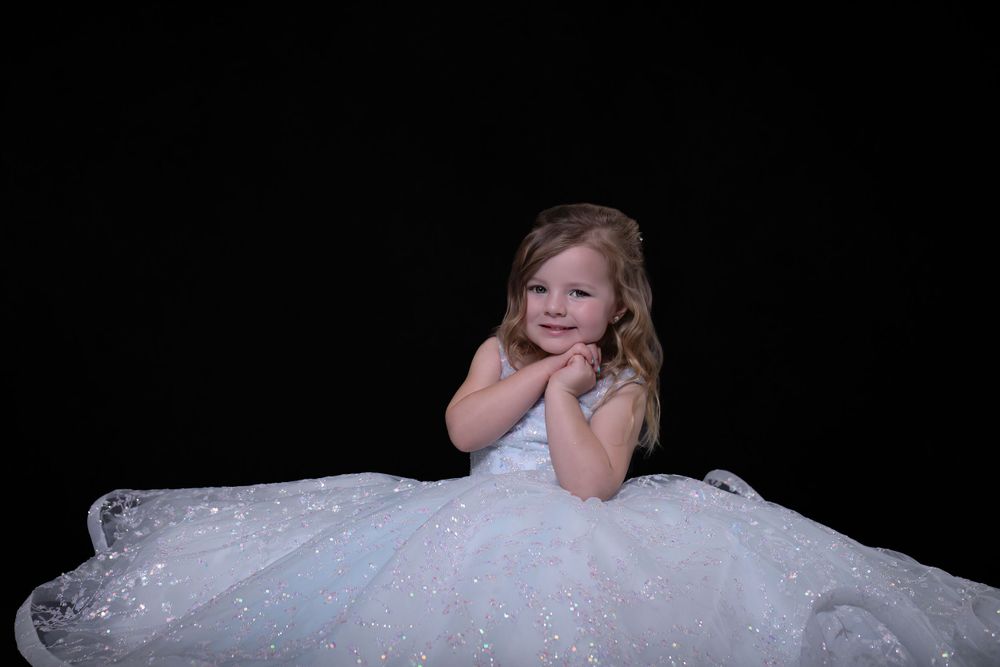 Portrait of young performer in white sparkly dress against black background.