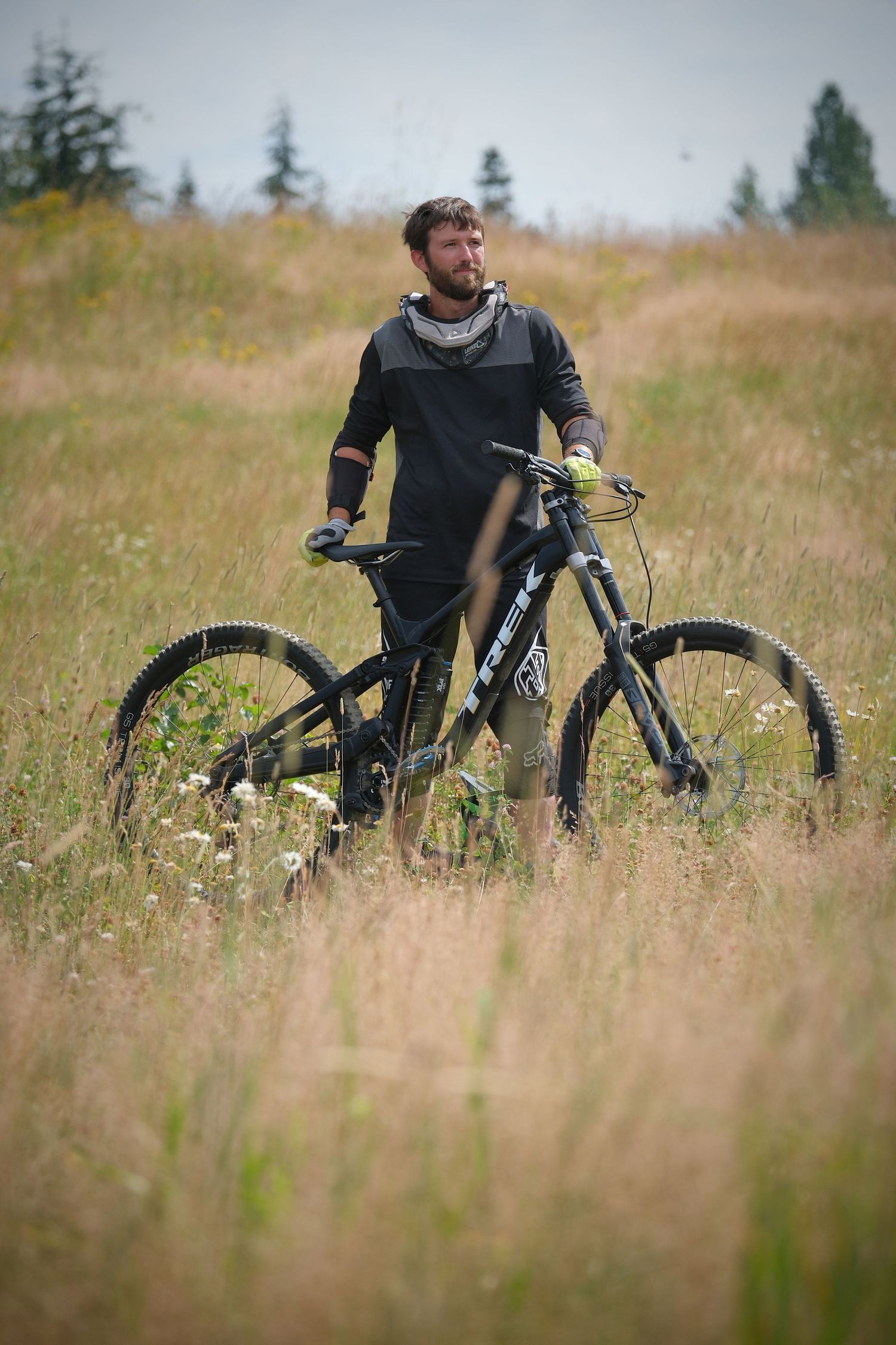 Mountain biker stands with bike in tall grass field with forest in background.
Whistler Mountain Bike Park