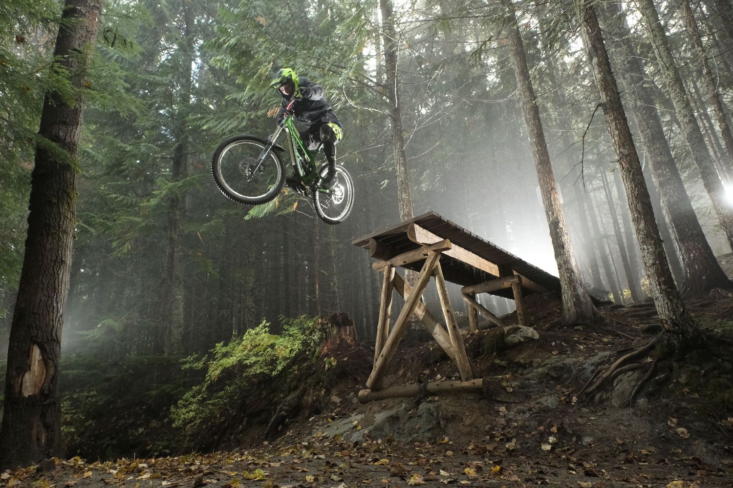 Mountain biker catches air off wooden ramp in atmospheric misty woods.
Whistler Mountain Bike Park