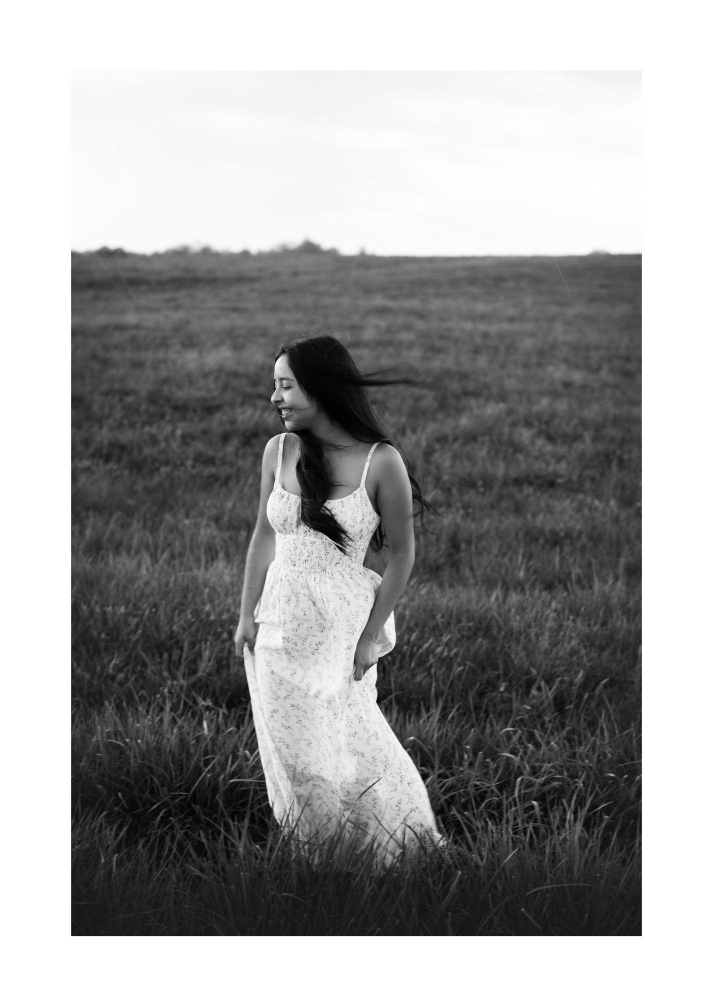 Black and white portrait of person in white dress standing in grassy field.