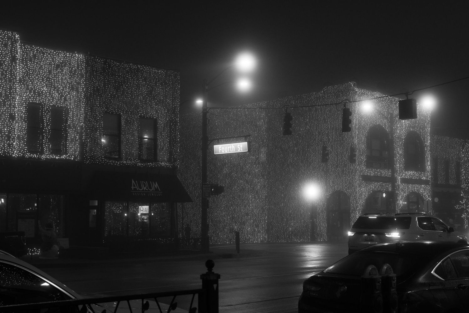 Historic brick buildings silhouetted against a foggy night sky with street lamps casting moody light.