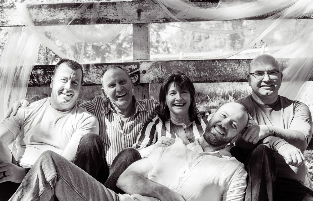 Black and white photo of five smiling adults posing together outdoors under a canopy.