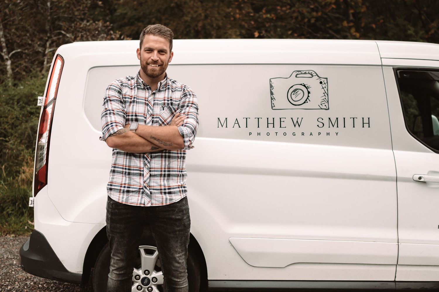 Professional photographer stands with crossed arms next to branded white van.