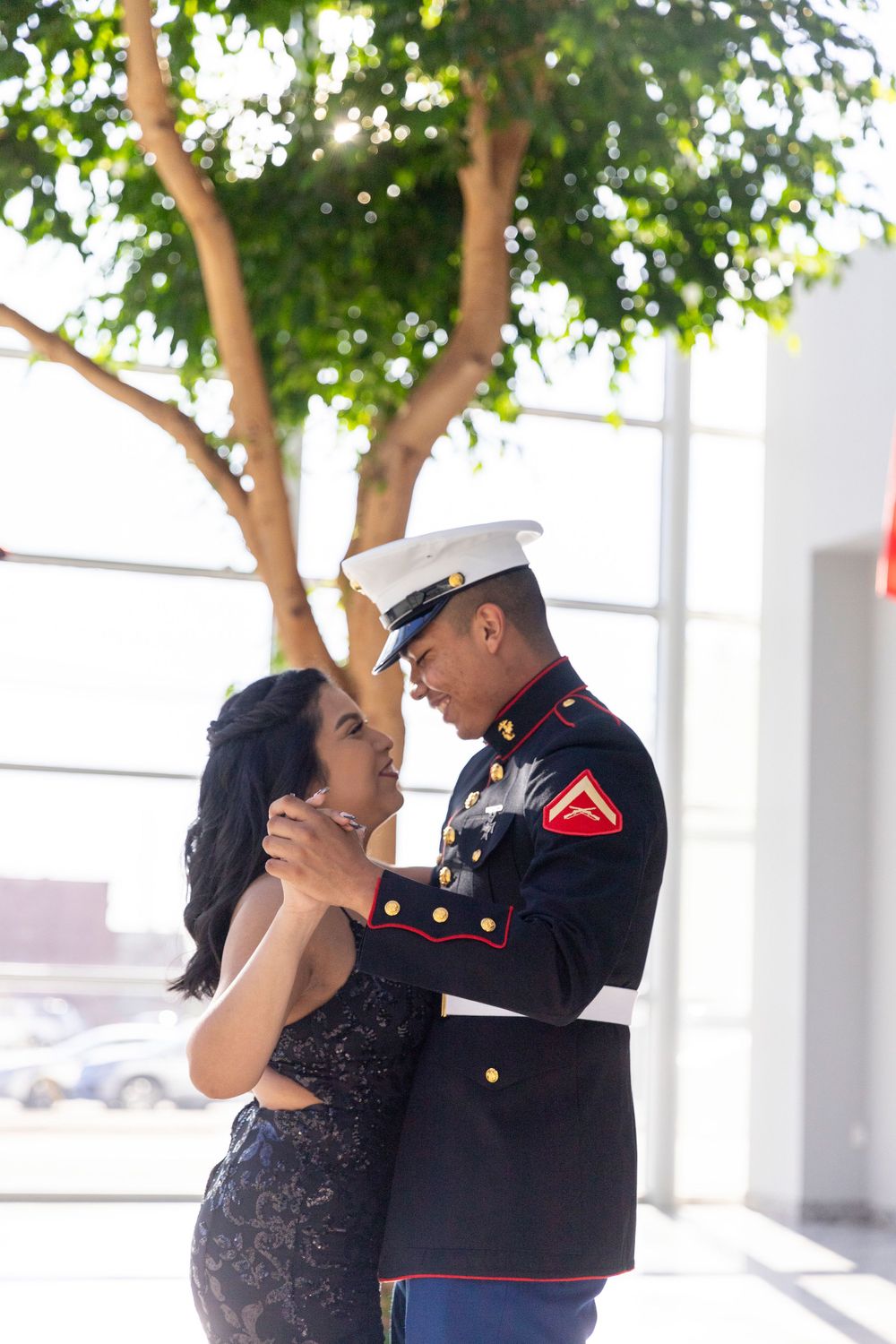 Marine in dress uniform and woman in dark dress share a romantic moment dancing beneath a tree.