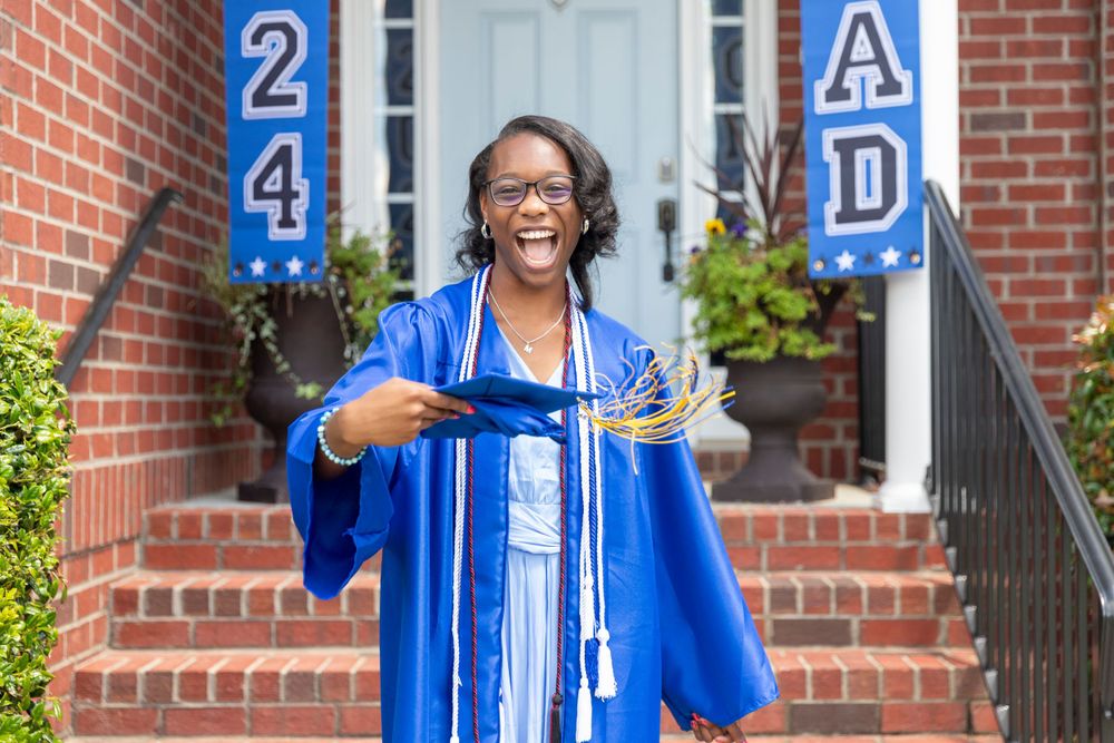 Graduate in bright blue cap and gown celebrates joyfully on brick steps with class numbers in the background.