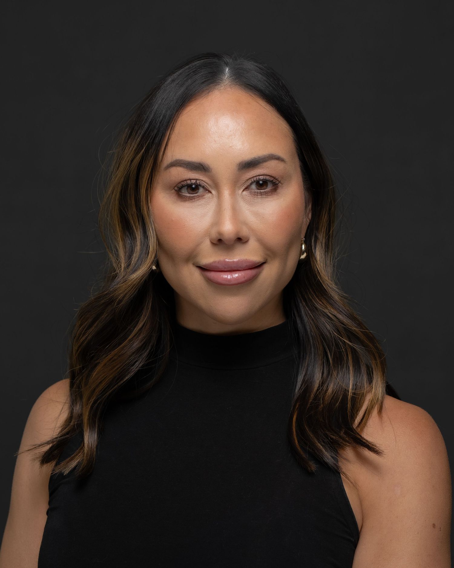 Professional headshot of woman in black sleeveless top with soft waves and pearl earrings