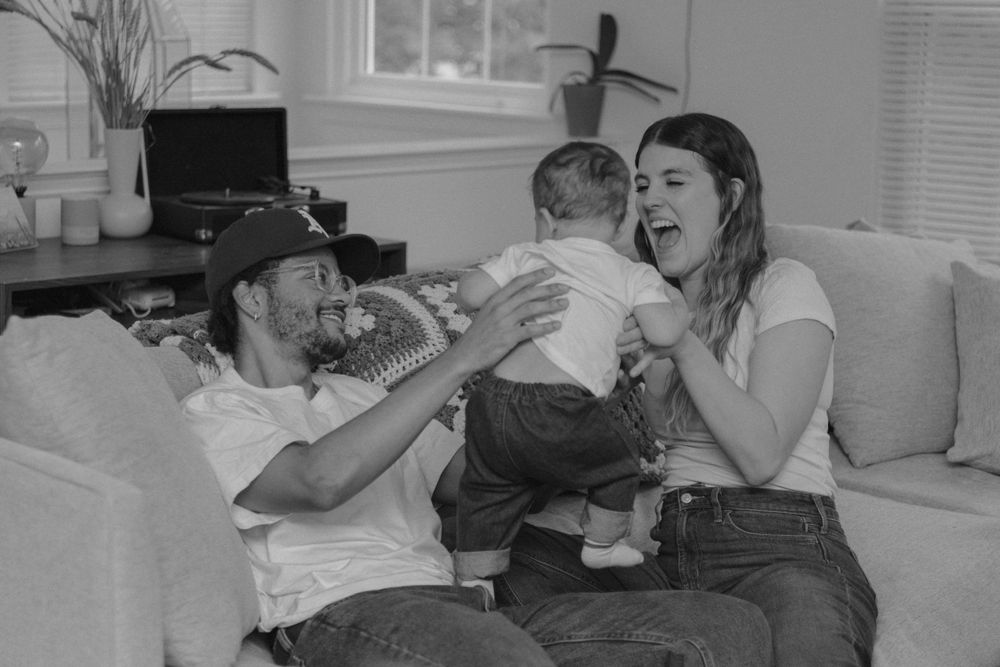 A playful family interaction captured in black and white on a cozy sofa.