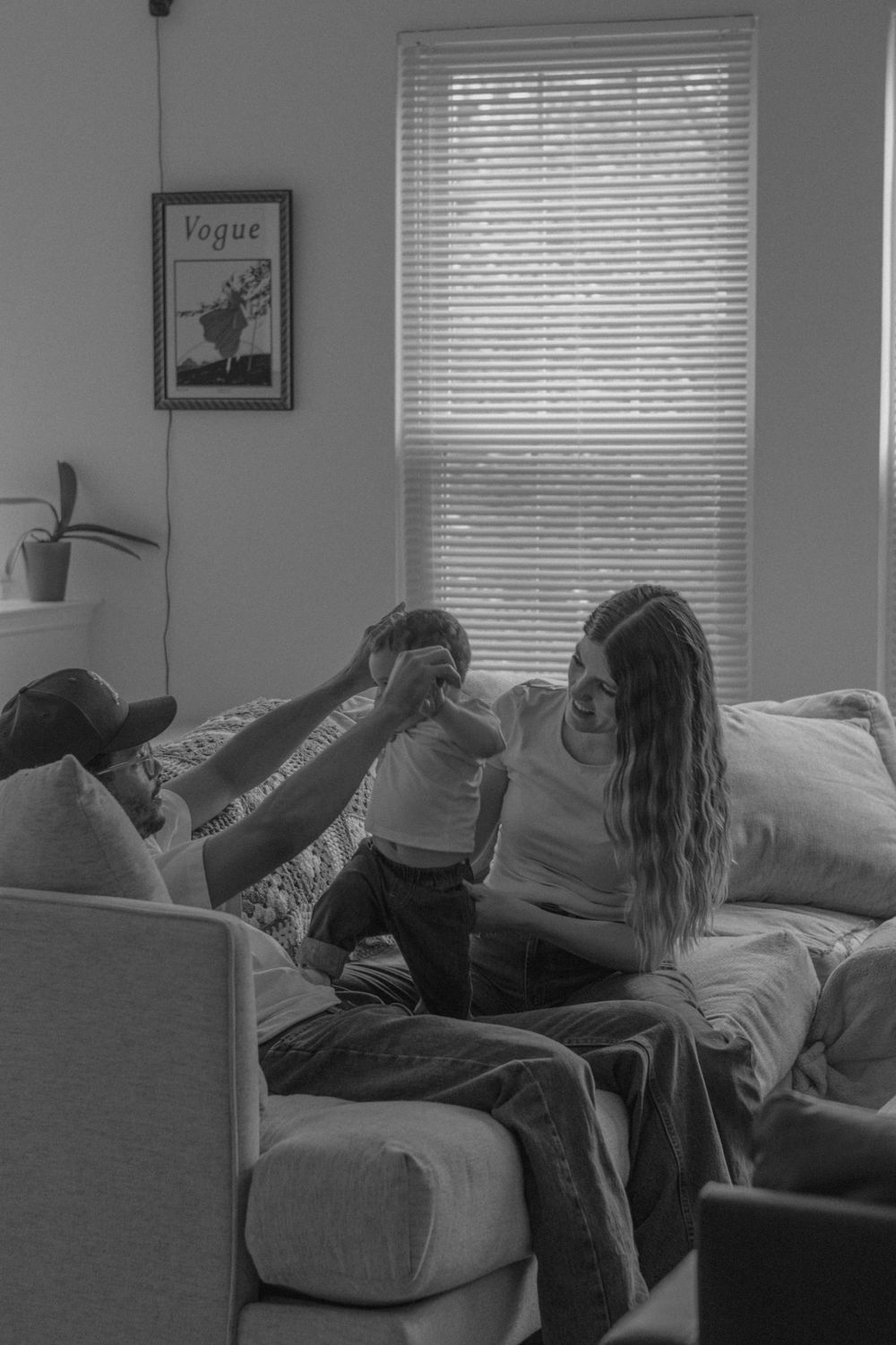 An intimate black and white family portrait with window light and a Vogue poster in the background.