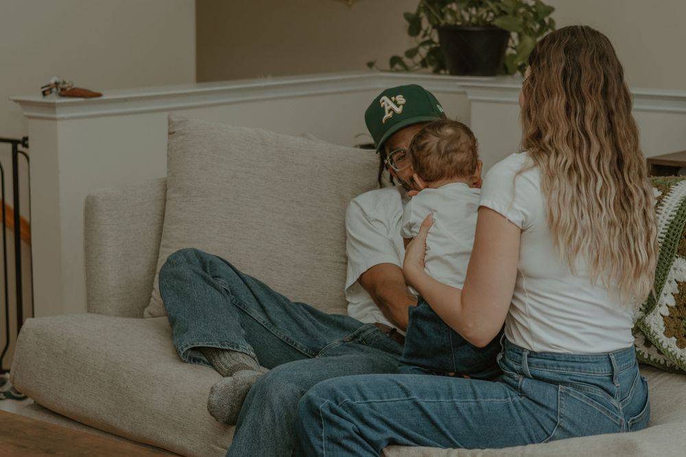 A tender family moment captured on a beige couch in warm, muted tones.