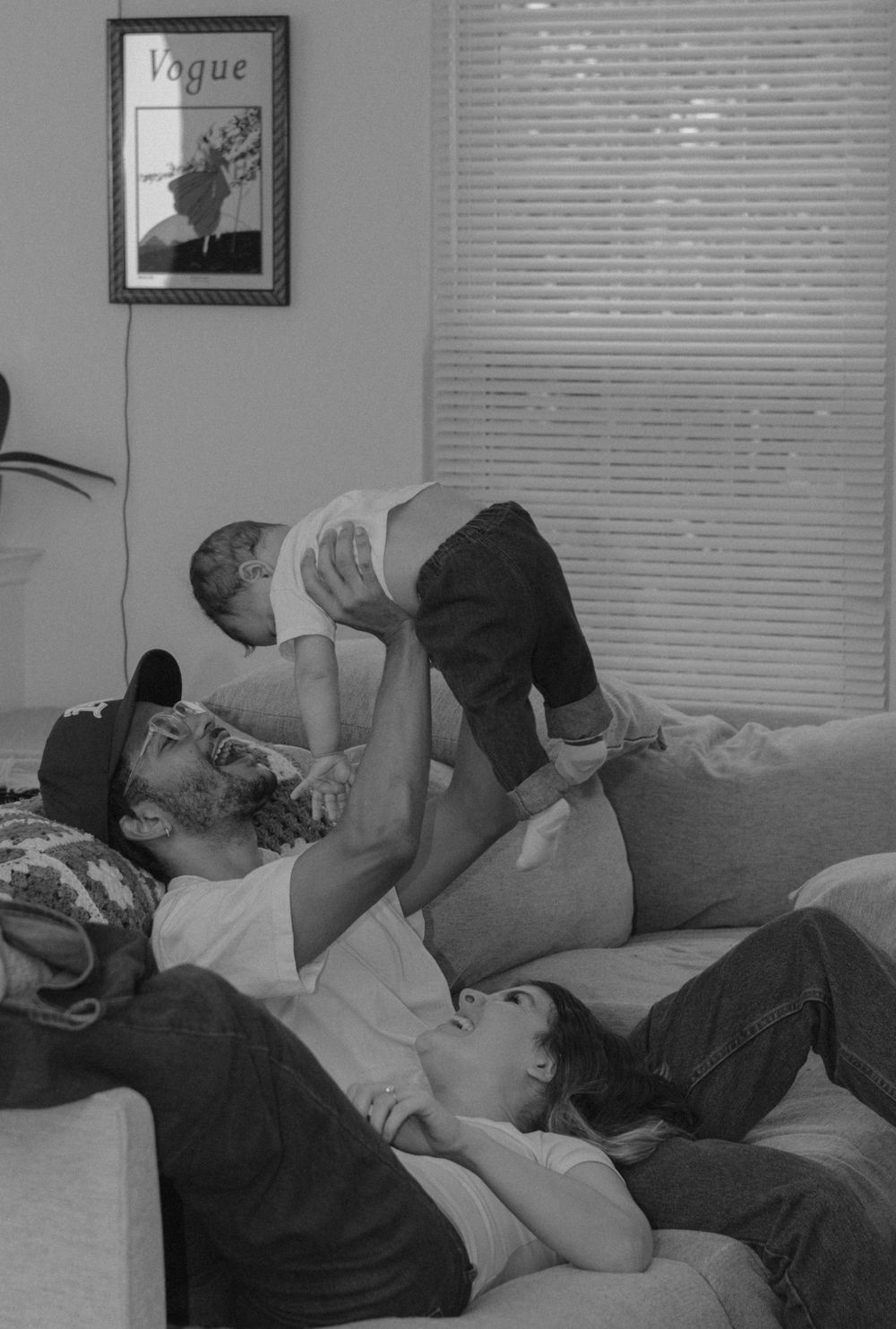 A black and white photo showing playtime between family members lounging on a sofa.