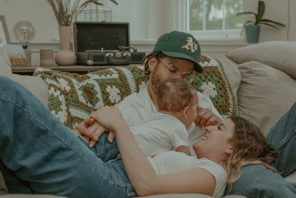 Cozy afternoon cuddles between parent in Oakland A's hat and child on living room sofa.