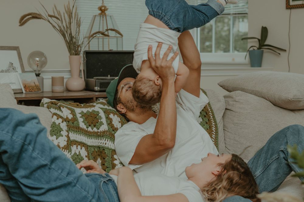 Joyful playtime scene of parent lifting child in air while lying on living room couch.