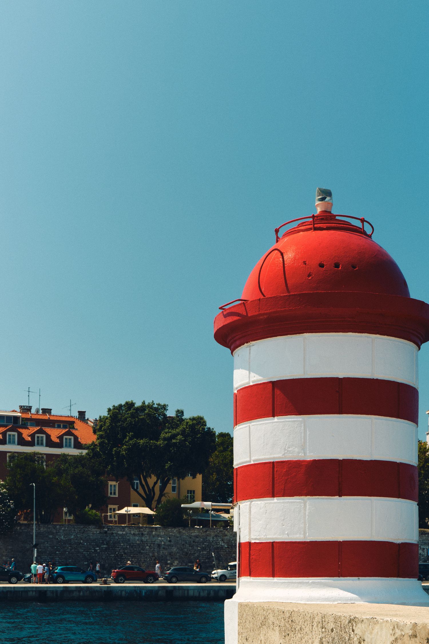 Red and white striped lighthouse tower against clear blue sky.