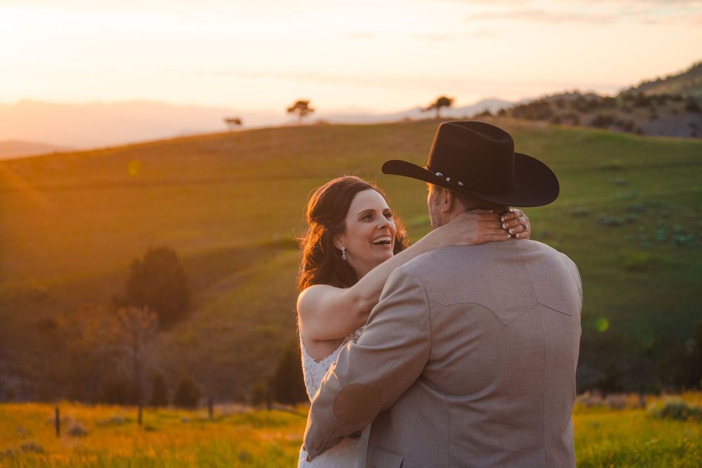 A couple shares an intimate moment at sunset in a grassy hillside landscape wearing western cowboy attire.
