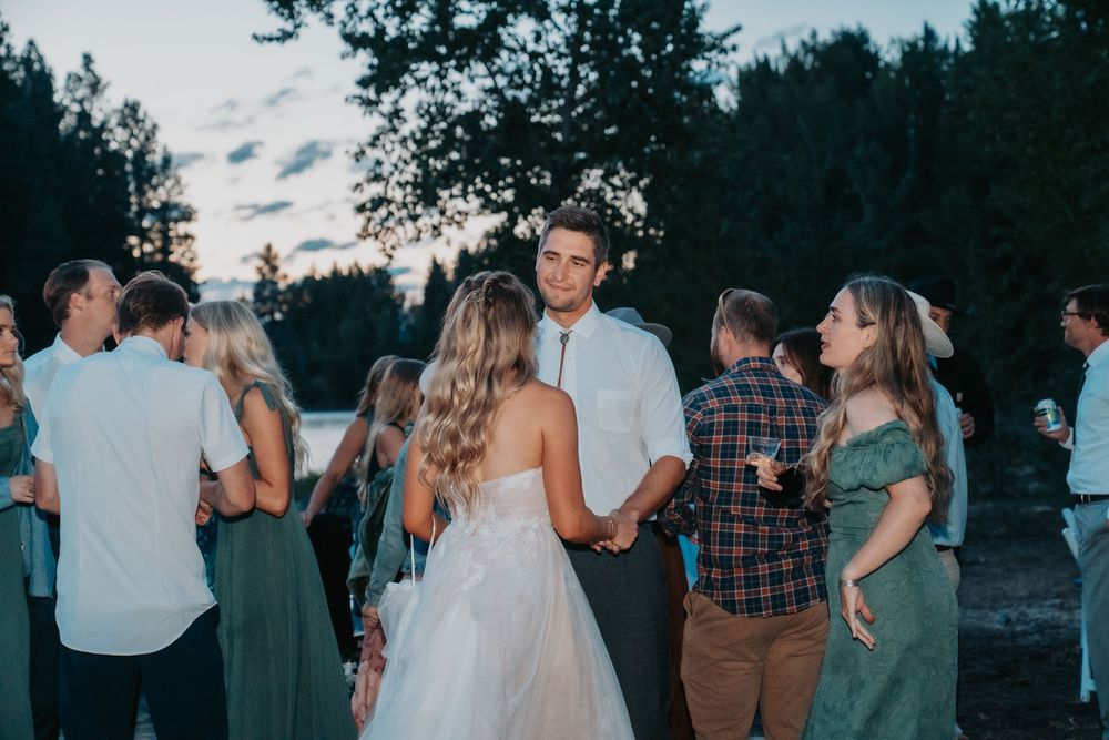 Group of wedding guests gather outdoors at sunset during a warm summer evening celebration.