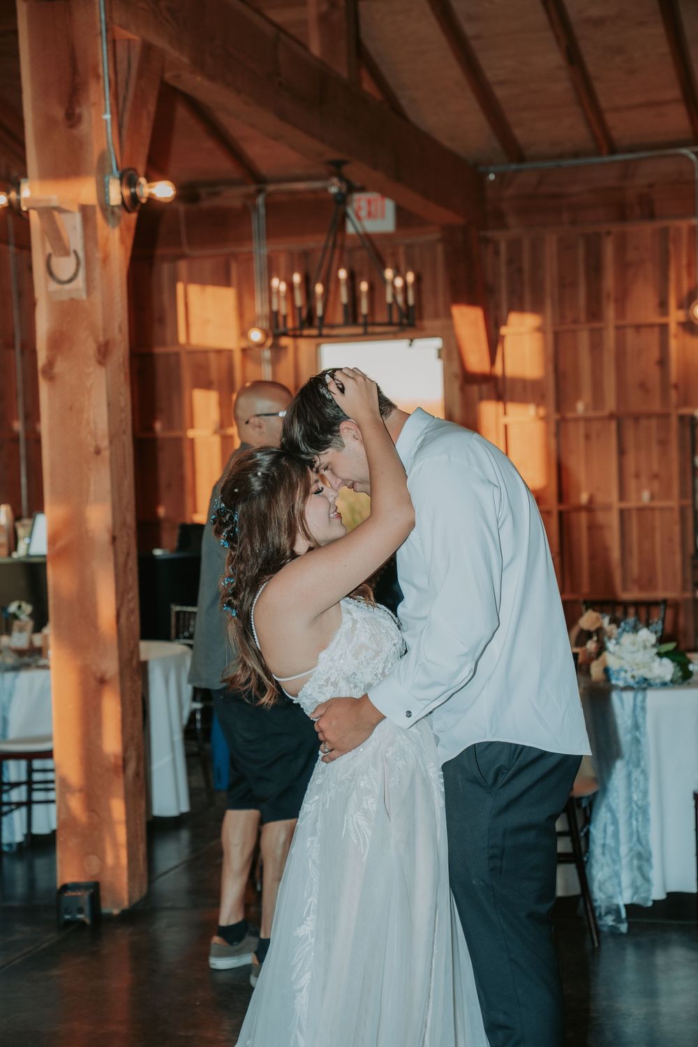 A couple shares their first dance as newlyweds in a rustic wooden barn reception venue with warm lighting.