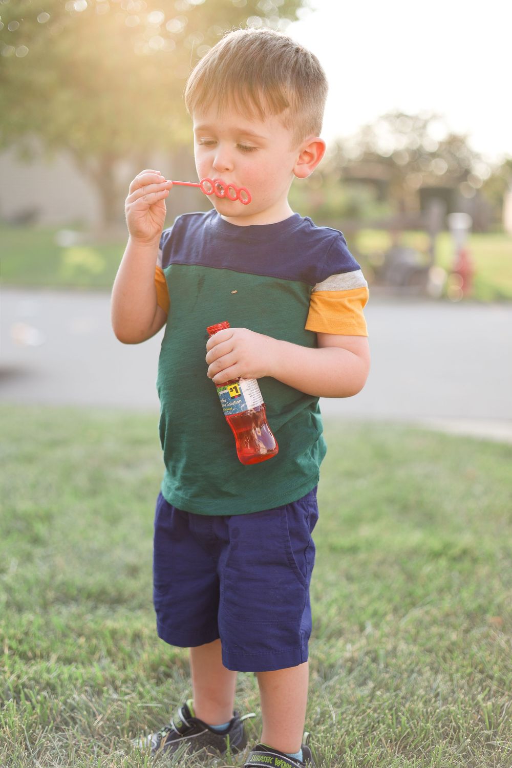 A child in colorful clothing blows bubbles while playing outdoors in a backyard.