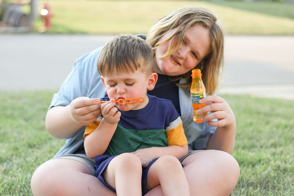 Two people enjoy time together blowing bubbles while sitting outside in warm sunlight.